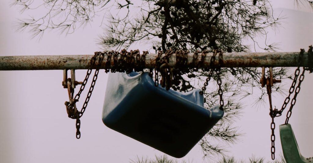 A rusty swing hangs from tree branches in a neglected playground, evoking a sense of nostalgia.