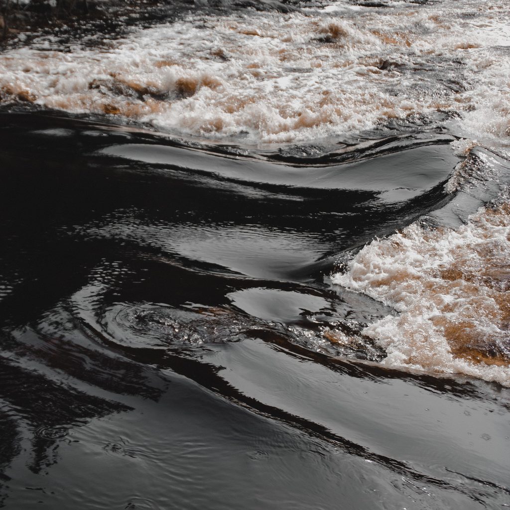 Smooth and dynamic river currents with foamy surface and a visible whirlpool, creating a captivating natural scene.